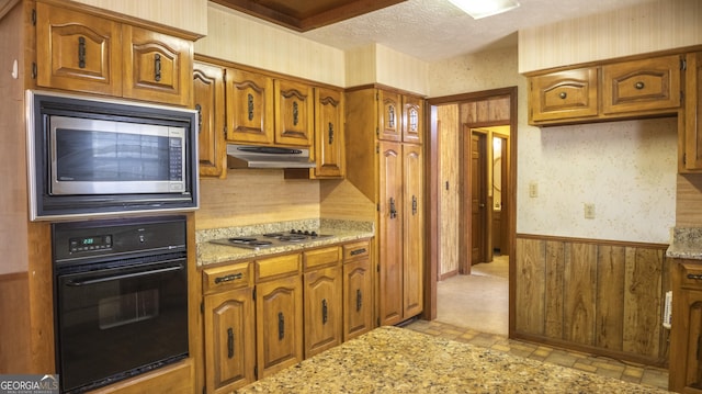 kitchen featuring wallpapered walls, wainscoting, stainless steel appliances, a textured ceiling, and under cabinet range hood