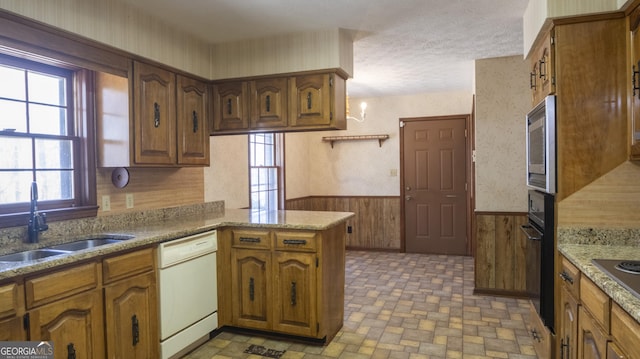 kitchen with wainscoting, brown cabinets, a peninsula, stainless steel appliances, and a sink