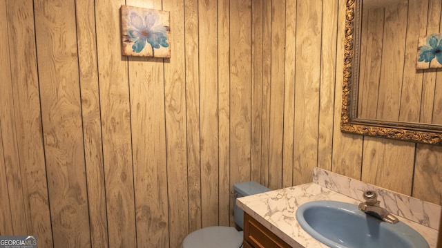 bathroom featuring toilet, wood walls, and vanity