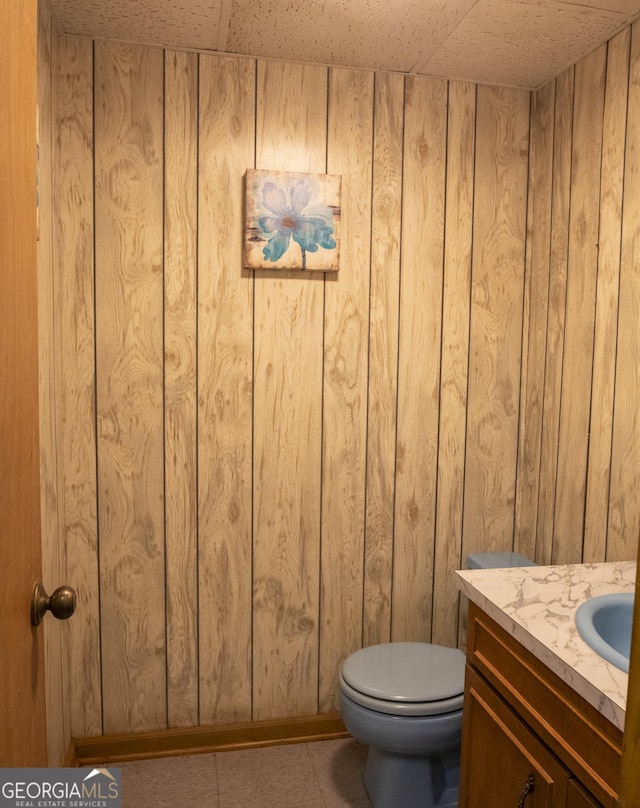 bathroom with tile patterned flooring, vanity, toilet, and wooden walls