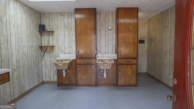 interior space with baseboards, a sink, wooden walls, and light floors