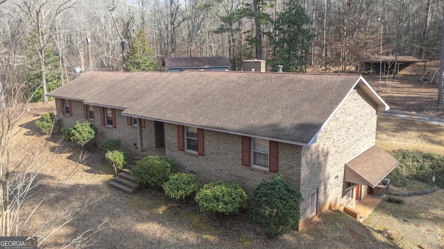 view of front of property with a shingled roof, a view of trees, and brick siding