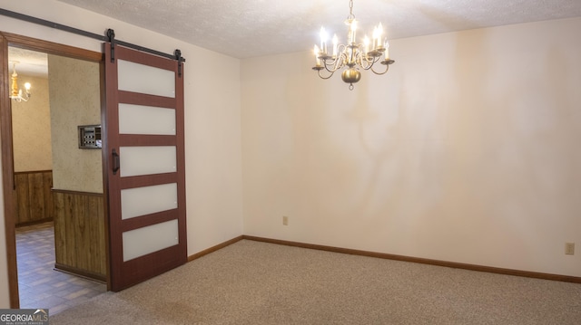 carpeted spare room with a chandelier, a textured ceiling, a barn door, wooden walls, and a wainscoted wall