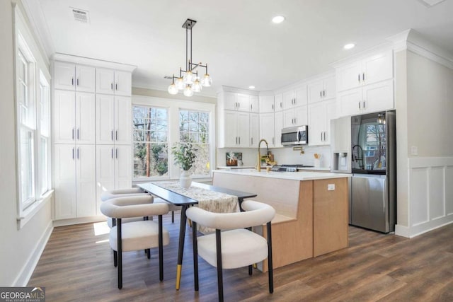 kitchen with stainless steel appliances, plenty of natural light, light countertops, and a center island with sink