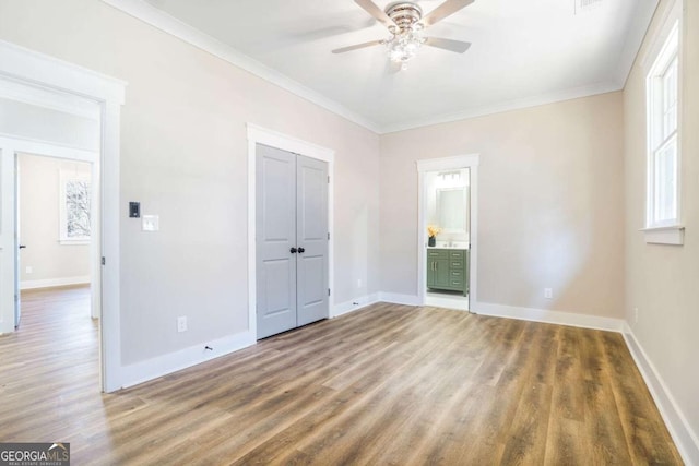 unfurnished bedroom featuring wood finished floors, baseboards, ornamental molding, a closet, and ensuite bath