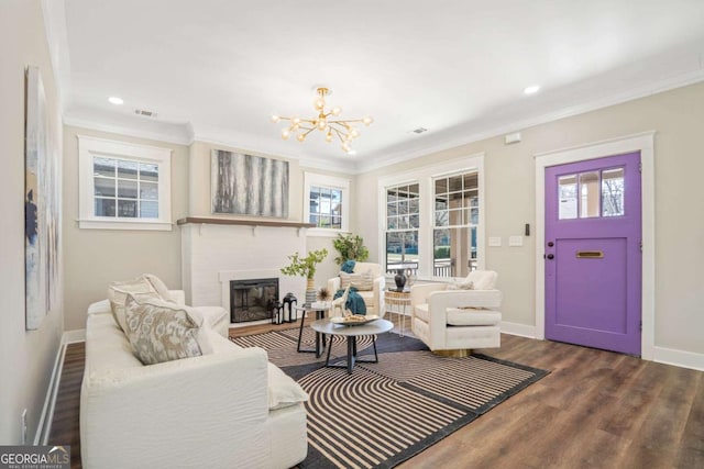 living room featuring baseboards, a glass covered fireplace, dark wood-style flooring, crown molding, and a chandelier