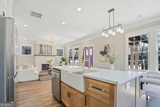 kitchen with a sink, appliances with stainless steel finishes, open floor plan, visible vents, and ornamental molding