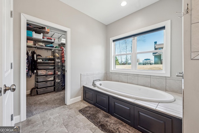 bathroom featuring a spacious closet, baseboards, and a bath