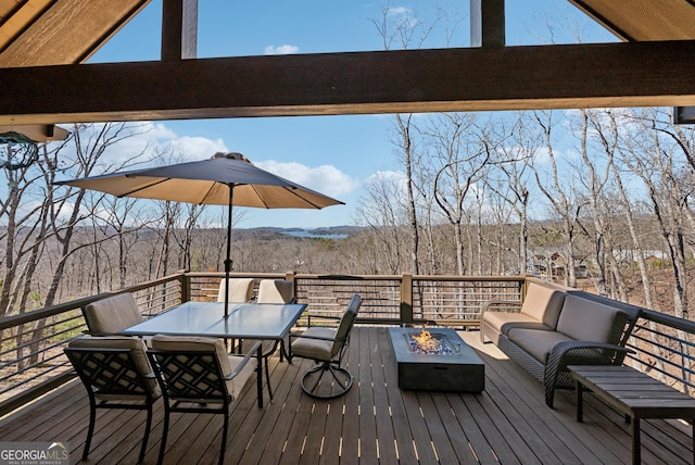 wooden deck with outdoor dining area, a wooded view, and an outdoor living space with a fire pit