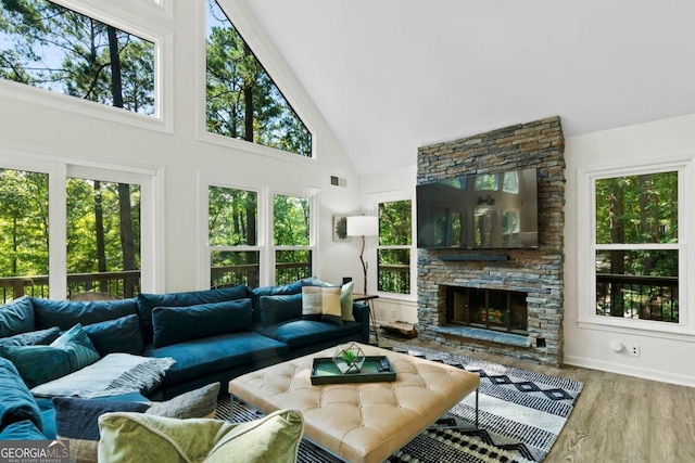 living area with high vaulted ceiling, visible vents, wood finished floors, and a stone fireplace