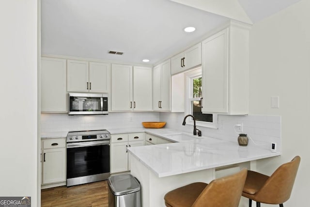 kitchen featuring stainless steel appliances, a peninsula, a sink, visible vents, and a kitchen breakfast bar