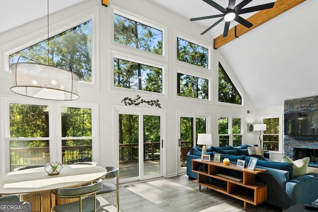 sunroom with vaulted ceiling with beams, a ceiling fan, and a stone fireplace