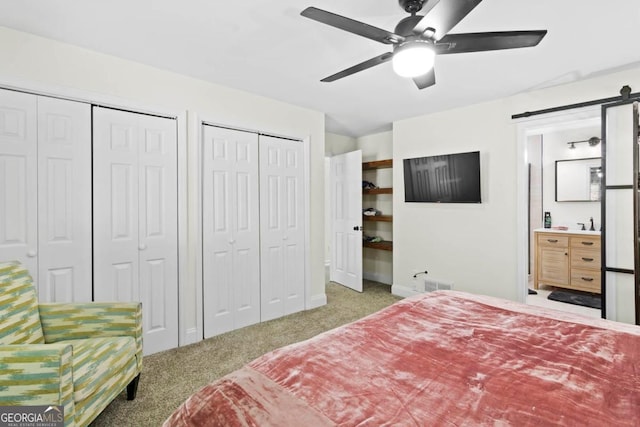 carpeted bedroom with a barn door, visible vents, a ceiling fan, ensuite bathroom, and two closets