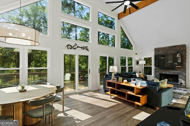 sunroom / solarium with ceiling fan, a stone fireplace, and lofted ceiling with beams