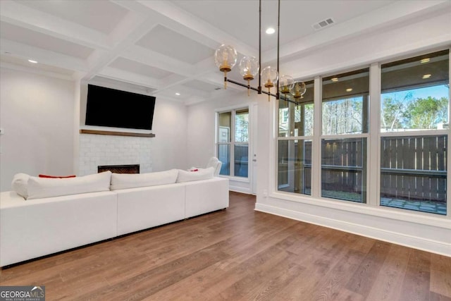 unfurnished living room featuring coffered ceiling, a fireplace, wood finished floors, visible vents, and beam ceiling