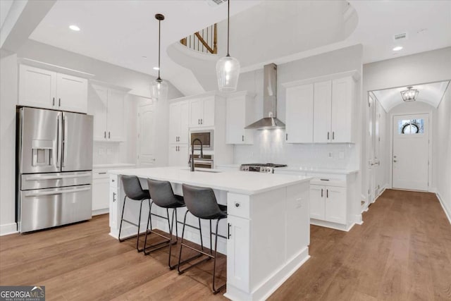 kitchen with wall chimney exhaust hood, stainless steel refrigerator with ice dispenser, a sink, and white cabinetry