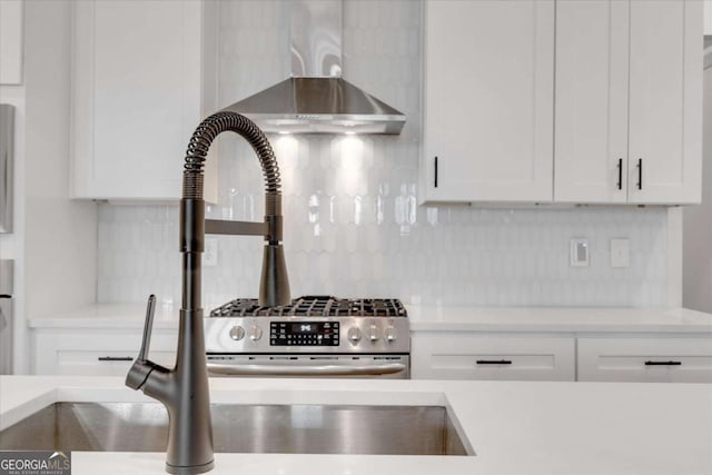 kitchen featuring wall chimney range hood, tasteful backsplash, and white cabinetry