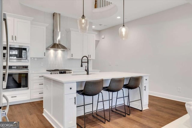 kitchen with wood finished floors, a sink, light countertops, wall chimney range hood, and appliances with stainless steel finishes