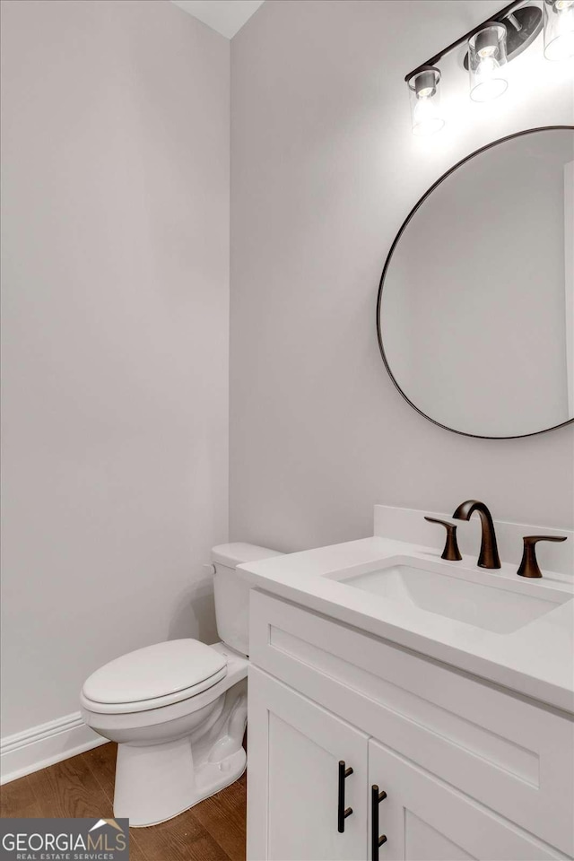 half bathroom with toilet, baseboards, wood finished floors, and vanity