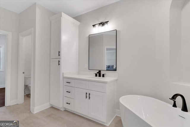 bathroom featuring baseboards, a freestanding bath, vanity, and toilet