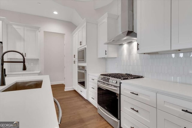 kitchen with white cabinets, appliances with stainless steel finishes, light countertops, wall chimney range hood, and a sink