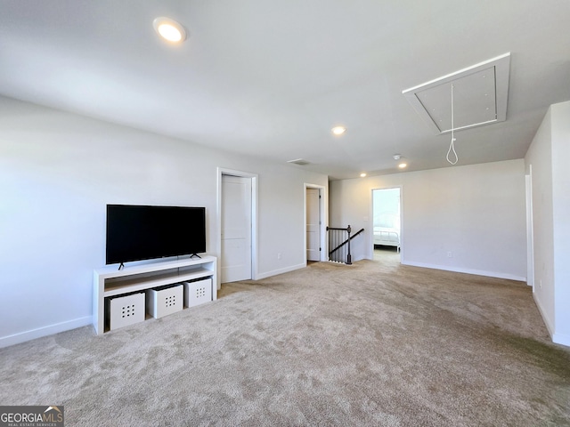 unfurnished living room featuring carpet flooring, attic access, and baseboards