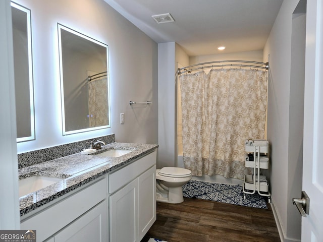 bathroom with double vanity, visible vents, toilet, a sink, and wood finished floors