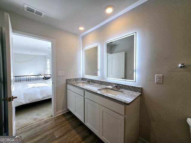 ensuite bathroom featuring double vanity, visible vents, a sink, and wood finished floors