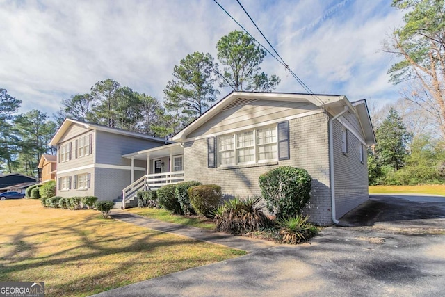 view of property exterior featuring covered porch, a yard, brick siding, and driveway