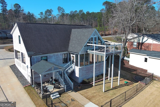 exterior space with roof with shingles, brick siding, stairway, fence, and a front lawn