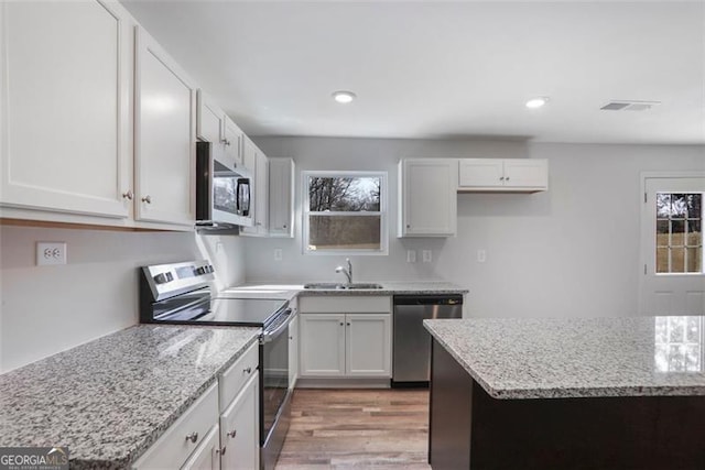 kitchen featuring white cabinets, light stone counters, stainless steel appliances, light wood-type flooring, and a sink