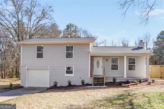 split level home with driveway, a chimney, an attached garage, fence, and stucco siding