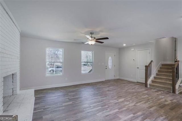 unfurnished living room featuring stairway, a brick fireplace, wood finished floors, and baseboards