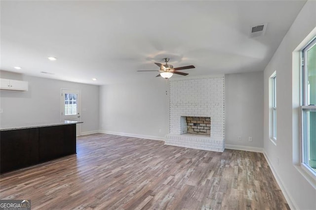 unfurnished living room featuring wood finished floors, a ceiling fan, visible vents, baseboards, and a brick fireplace