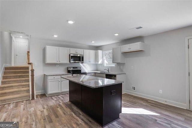 kitchen featuring white cabinets, a kitchen island, wood finished floors, light stone countertops, and stainless steel appliances