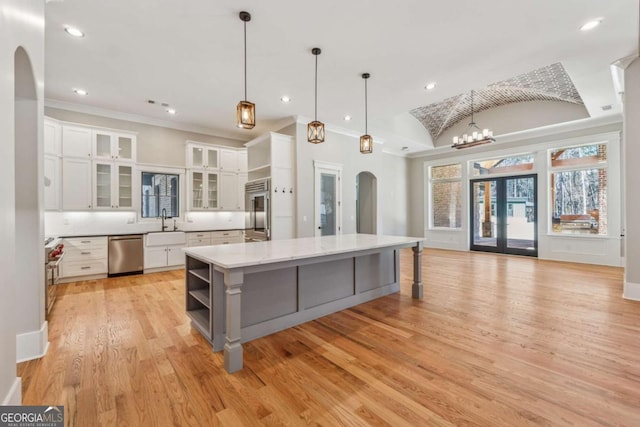 kitchen with arched walkways, white cabinets, light wood-style flooring, a large island, and appliances with stainless steel finishes