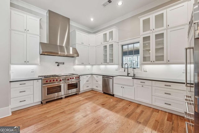 kitchen featuring crown molding, visible vents, appliances with stainless steel finishes, light wood-style floors, and wall chimney range hood