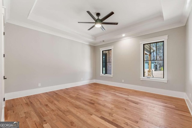 unfurnished room with light wood-type flooring, baseboards, a raised ceiling, and crown molding