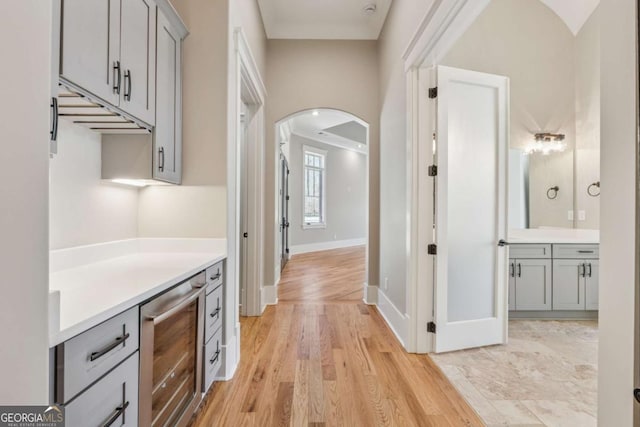 bar featuring wine cooler, baseboards, arched walkways, and light wood finished floors