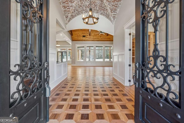 entrance foyer with brick ceiling, vaulted ceiling, a decorative wall, and an inviting chandelier