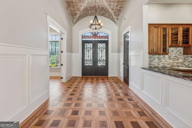 entrance foyer featuring french doors, a wainscoted wall, an inviting chandelier, vaulted ceiling, and brick ceiling