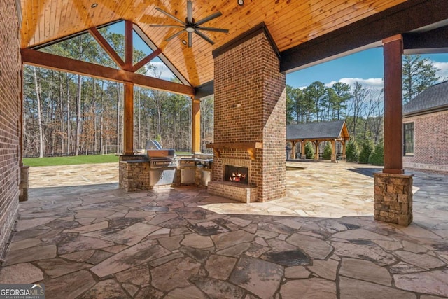 view of patio with an outdoor brick fireplace, a ceiling fan, area for grilling, exterior kitchen, and a gazebo