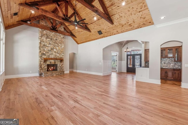 unfurnished living room featuring arched walkways, light wood finished floors, a stone fireplace, high vaulted ceiling, and wooden ceiling