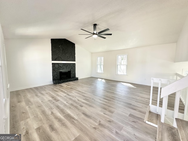 unfurnished living room featuring lofted ceiling, a fireplace, wood finished floors, a ceiling fan, and stairs