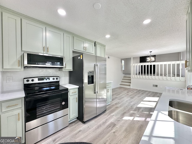 101 Summer Pond Trl, Lawrenceville, GA 30046 - kitchen with appliances with stainless steel finishes, a textured ceiling, light countertops, light wood finished floors, and tasteful backsplash