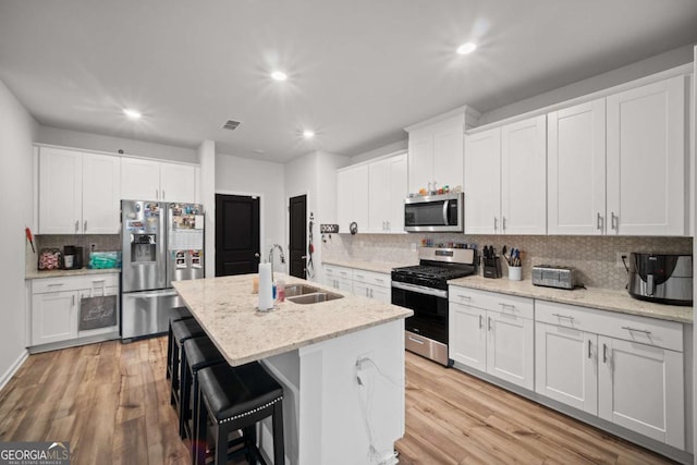 kitchen with stainless steel appliances, a sink, a center island with sink, and light wood-style floors