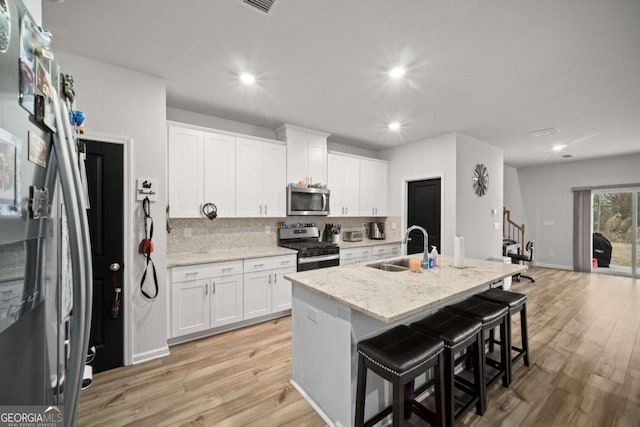 kitchen featuring light wood finished floors, appliances with stainless steel finishes, a sink, and decorative backsplash