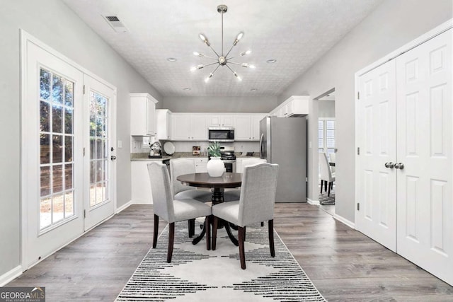 dining space with a chandelier, wood finished floors, visible vents, and baseboards