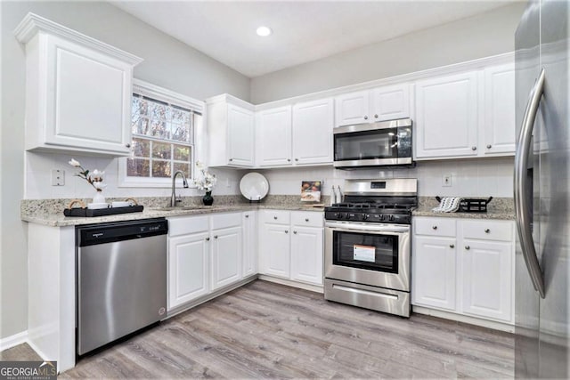 kitchen with stainless steel appliances, a sink, white cabinetry, light stone countertops, and light wood finished floors