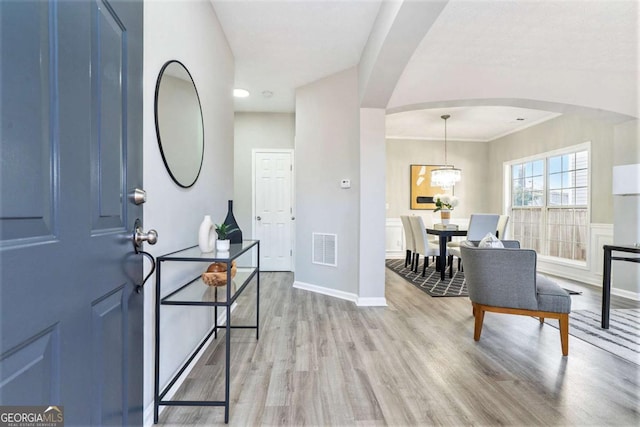 foyer with light wood-style floors, baseboards, visible vents, and arched walkways